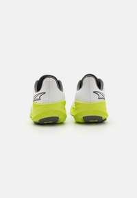 White and gray athletic shoes with a bright yellow sole, featuring textured material and distinctive logo on the back.