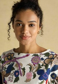 Bluzka w kwiatowy wzór z białym tłem, z misternym niebieskim, różowym i zielonym haftem. Okrągły dekolt i krótkie rękawy.
