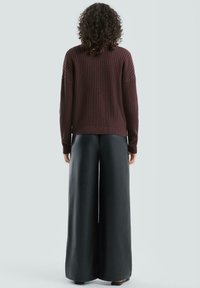 Bordowy sweter dziany z fakturowanym wzorem i prążkowanym ściągaczem, w zestawie z szerokimi czarnymi spodniami. Tkanina wydaje się miękka, a fason luźny i wygodny.