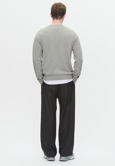 Grå sweater med ribbet kant, båret over en hvid skjorte, parret med løstsiddende mørke bukser og grå sneakers. Set bagfra.