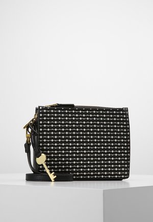 Black crossbody bag with white dotted line pattern, gold zipper, and a gold key charm attached to the strap, placed on a white surface.
