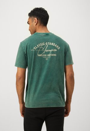 Türkisfarbener Baumwoll-T-Shirt mit Rundhalsausschnitt und kurzen Ärmeln, mit einem grafikmäßigen Druck "Classic Standard Champion" in Beige auf der Rückseite.