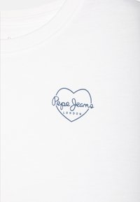 Valkoinen puuvillainen t-paita, jossa on sininen sydämenmuotoinen logo, jossa lukee "Pepe Jeans" ja "LONDON". Lyhyet hihat ja pyöreä pääntie.