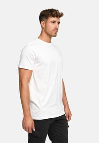 White cotton t-shirt with a round neckline, short sleeves, and a subtle logo on the chest, paired with black pants featuring pockets.