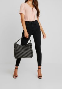 mustekka kudottu käsilaukku, jossa on kaareva muoto, mustat kapeat farkut ja vaaleanpunainen lyhythihainen paita, jossa on avainaukko-yksityiskohta.