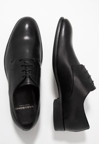 Scarpe eleganti in pelle nera con finitura liscia, design allacciato, punta rotonda e tacco piatto. Presentano cuciture sottili e il logo del marchio all'interno.