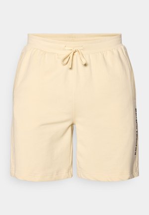 Shorts en coton beige avec taille élastique, cordon de serrage et poches latérales. Présente un texte imprimé le long de la jambe gauche.