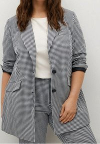 Czarnobiała marynarka w kratę gingham z dwoma przednimi kieszeniami, zapięciem na jeden guzik, podwiniętymi rękawami i gładką białą bluzką pod spodem.