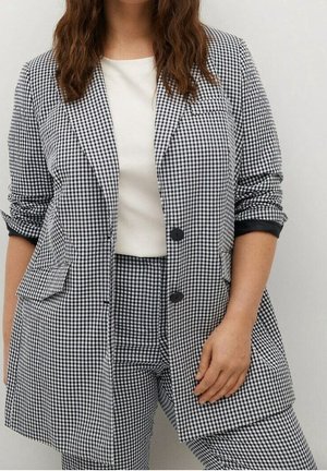 Zwart-wit geruite blazer met twee voorzakken, enkele knoopsluiting, opgerolde mouwen en een gladde witte top eronder.