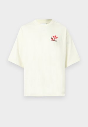 Väriltään maitomaisen valkoinen, lyhythihainen T-paita pyöreällä pääntiellä ja pienellä punaisella Adidas-logolla, jossa on chili-kuvitus vasemmalla rinnalla.