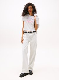 Graues, kürzer geschnittenes T-Shirt mit farbenfrohem "Tommy Jeans"-Logo, kombiniert mit locker sitzenden, cremefarbenen Jeans und schwarzen Plateauschuhen.