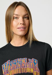 Camiseta de algodón negra con un colorido logo "WRANGLER" en tipografía retro y en negrita. Manga corta y escote redondo.