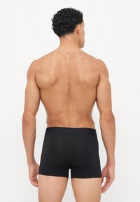 Boxer shorts en coton noir avec une taille lisse, design ajusté et sans motifs visibles. Modèle vu de dos, peau nue visible.