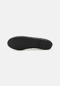 Semelle de chaussure en caoutchouc noir avec un motif tissé texturé, des bords lisses et un logo de marque embossé dans la zone du talon.
