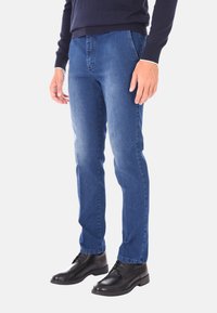 Jeans in denim blu scuro, cinque tasche, design aderente, leggero sbiadimento sulle cosce, abbinati a scarpe di pelle nere eleganti.