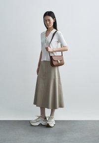 Valge soonikuga lühikeste varrukatega top pitsist nöörist kaelusega, beež A-lõikelise seelikuga ja beežid tossud hallide detailide ja valge tallaga. Pruun õlakott.