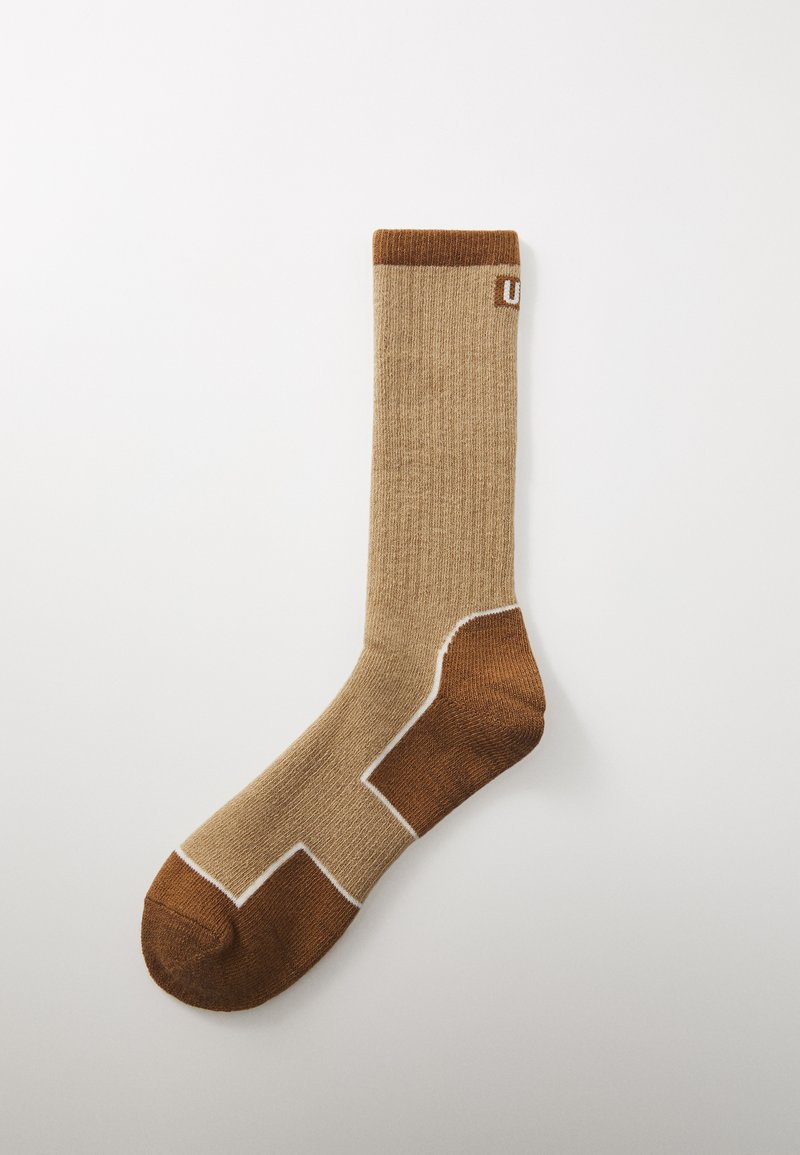Bruna strumpor med en strukturerad yta, som har en vit accentlinje och en enfärgad mörkbrun häl. Enkel design, medelhöjd.