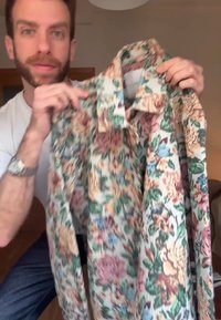 Camisa de estampado floral en tela de algodón, con una base blanca y flores en tonos rosa, azul y verde. Mangas largas y diseño de cuello clásico.
