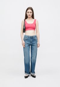 Top cropped rosa justo com alças largas, combinado com jeans azuis claros de perna reta. Sapatos baixos pretos completam o conjunto. Fundo liso.