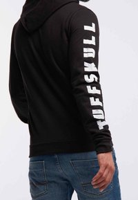 Felpa nera con cappuccio con la scritta "TUFFSKULL" stampata in grandi lettere bianche lungo la manica sinistra; presenta un tessuto strutturato e una vestibilità aderente.