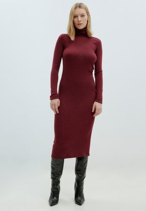 Robe mollet en bordeaux, col roulé, en tissu élastique, ajustée, à manches longues, associée à des bottes noires à talons pointus montantes.