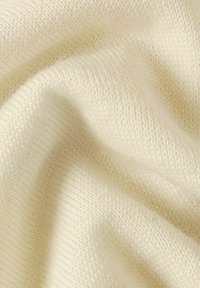 Tessuto a maglia morbido e leggero di colore crema, caratterizzato da una texture liscia con costine visibili e sottili variazioni di spessore.