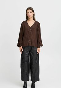 Brun, texturerad långärmad blus med V-ringning och knappar fram, ihopparad med svarta, vida faux läderbyxor.