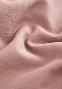 Tessuto rosa chiaro con una superficie liscia e leggermente texture, che mette in mostra pieghe e drappeggi delicati, indicando flessibilità e morbidezza.