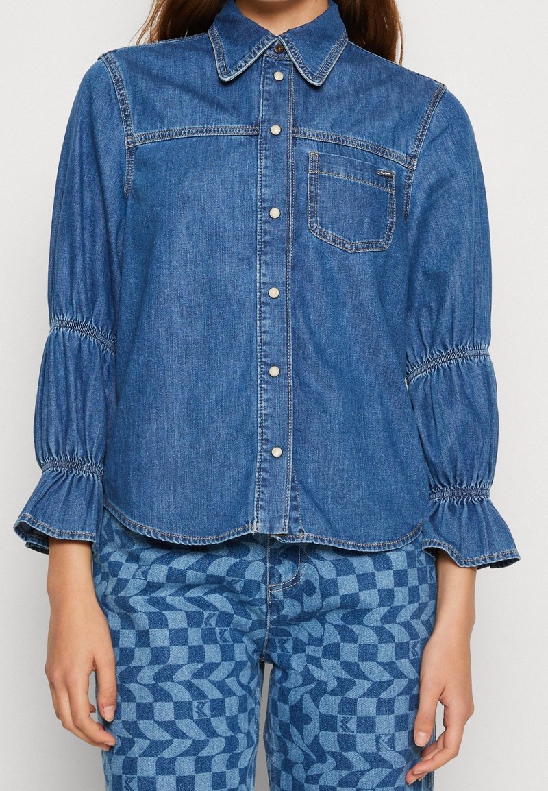 Jeansskjorta med knappstängning, klassisk krage och samlade ärmar. Har en ficka med lappar och diskreta sömnadsdetaljer. Blå färg.