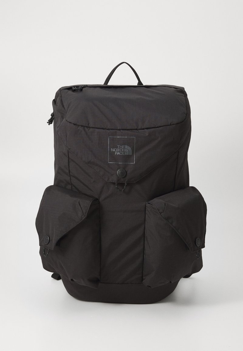 Sac à dos noir North Face avec trois poches avant, fermetures à rabat et une poignée supérieure, présenté sur un fond uni.
