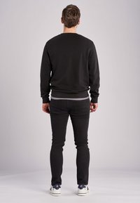 Felpa nera con collo girocollo, polsini e orlo a coste. Abbinata a jeans neri e sneakers bianche con dettagli blu. Design semplice.
