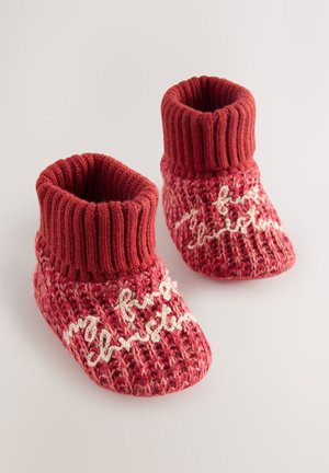 Chaussons pour bébé tricotés rouges avec une bordure côtelée, arborant un texte crème indiquant "mon premier Noël", motif texturé sur le corps.