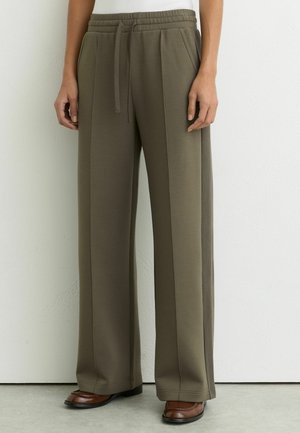 Pantalon vert olive à jambes larges avec taille à cordon, poches latérales et coutures avant surpiquées, porté avec des mocassins marron.