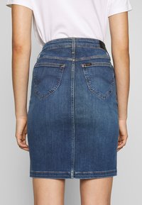 Jeanskjol i mörkblått med en figursydd design, medellång nederkant, bakfickor och subtila sömnadsdetaljer. Ren finish vid nederkanten.