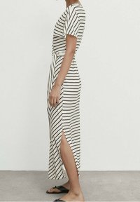 Randig midiklänning i krämfärgad och svart, med korta ärmar, en sidoklyvning och knytskärp i midjan. Materialet verkar mjukt och lätt.