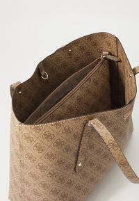 Sac fourre-tout marron à motifs en matériau texturé, avec une poche zippée intérieure et un logo sur un côté.