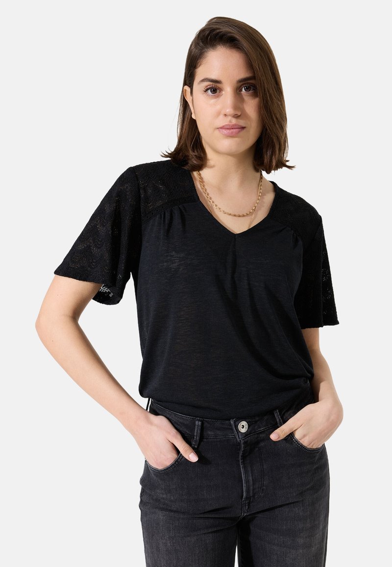 Schwarzes V-Ausschnitt-T-Shirt mit kurzen Spitzenärmeln, weichem Stoff und lässiger Passform, kombiniert mit dunklen Jeans.