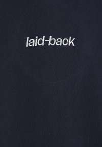 Námorná bavlnená tkanina s hladkou textúrou má na strede vyšívané slovo "laid-back" bielou niťou.