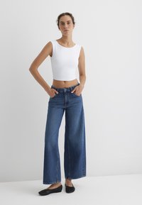 White sleeveless crop top paired with high-waisted wide-leg blue jeans and black woven flat shoes. Smooth texture and casual fit.