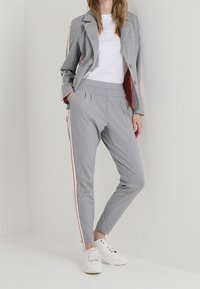 Grå kavaj och byxor med rosa sidostråk, med en slät textur. Matchad med en vit t-shirt och vita sneakers.