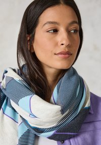 Écharpe multicolore avec des motifs géométriques bleus, blancs et gris foncé. Tissu doux avec une apparence texturée et confortable enroulée autour du cou.