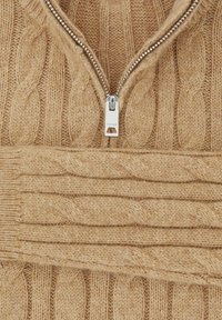 Pull en maille cable beige avec une fermeture éclair argentée partiellement descendue au niveau du col, montrant des motifs et textures de tricot détaillés.