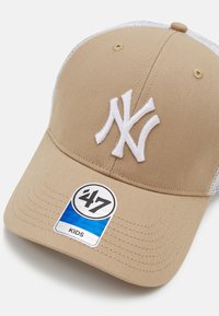 Beige Baseballcap mit weißem New York Yankees Logo, Netzrücken und verstellbarem Riemen. Mit einem runden '47' Etikett mit der Aufschrift "KIDS".