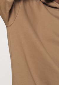 Tessuto marrone e morbido con una superficie liscia. Il design presenta una vestibilità ampia e un cappuccio, con dettagli di cucitura lungo le cuciture.