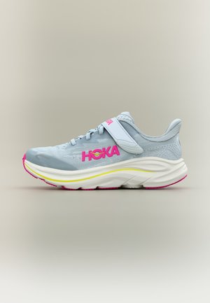 Lichtgrijze sportschoen met roze HOKA-logo, witte en gele tussenzool, roze buitenzool en een klittenbandsluiting op een neutrale achtergrond.
