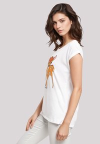 White cotton T-shirt featuring an orange cartoon deer graphic. Short rolled sleeves and a relaxed fit. Paired with light-colored pants.
