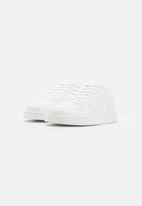 Weiße Sneaker aus synthetischem Material, mit glatter Textur, runder Zehenpartie und flacher Gummisohle mit Perforationen an den Seiten.