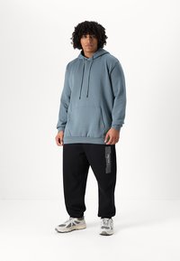Light blue hooded sweatshirt with a front pocket, paired with black sweatpants featuring a white logo and stripes, and gray sneakers.