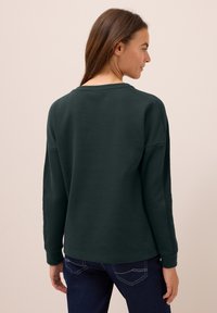 Mörkgrön sweatshirt i mjukt material, med en avslappnad passform, långa ärmar och rund halsringning. Utsmyckad med ribbade ärmmuddar.