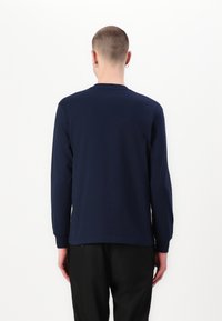 Chemise à manches longues bleu marine en coton, avec un col rond et des poignets côtelés, présentée sur une personne faisant face à l'envers sur un fond blanc.
